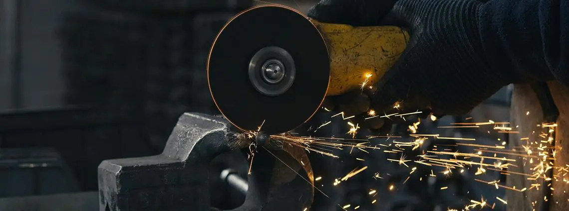 Angle grinder throwing sparks while cutting steel held in a vise