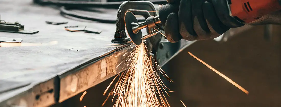 Grinder throwing sparks along the edge of a steel plate